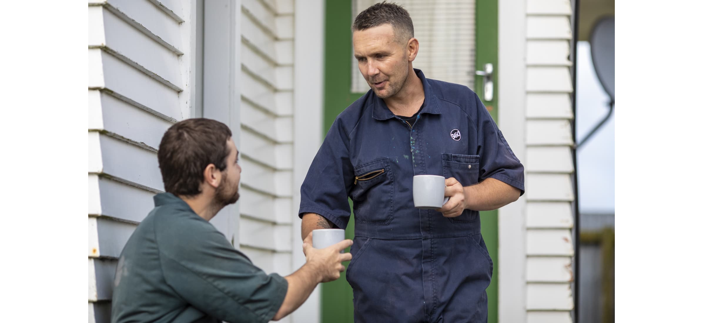 Simon hands employee Tomas a cup of tea outside a home.